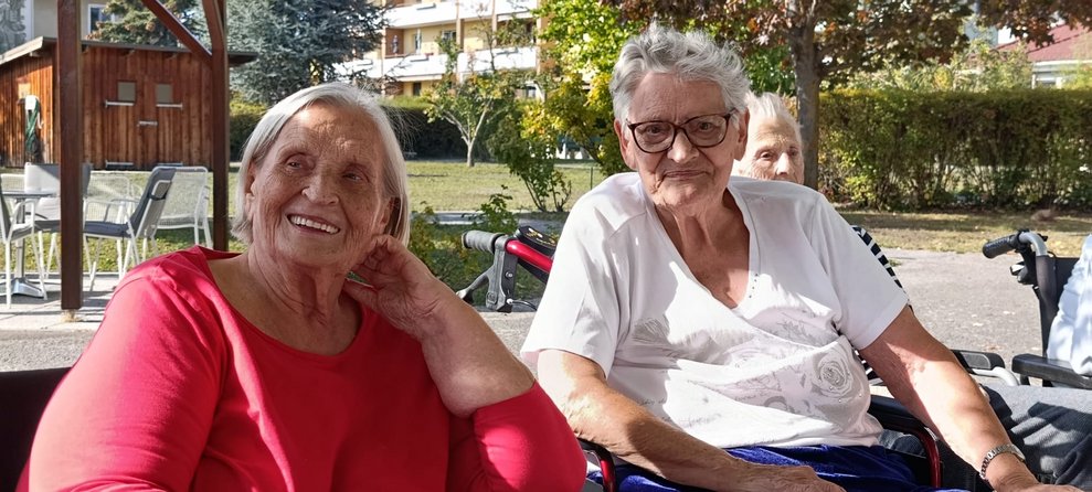Zwei lächelnde Bewohnerinnen im Rollstuhl in unserem Garten.