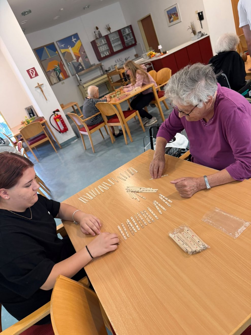 Bewohnerin und Schülerin beim Spielen. Viele Holzstangerl liegen auf Tisch.