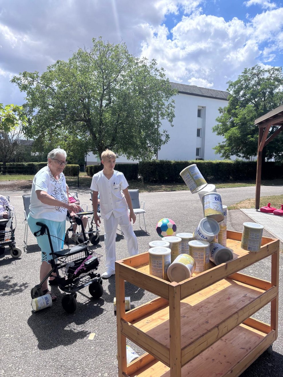 Bewohnerin beim Dosenschießen. Ball trifft Dosen. Mann (FSJ) steht daneben.