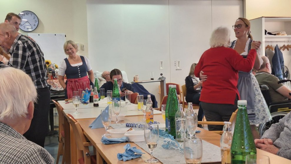Personen beim Oktoberfest. Mitarbeiterin und Bewohnerin tanzen zusammen.