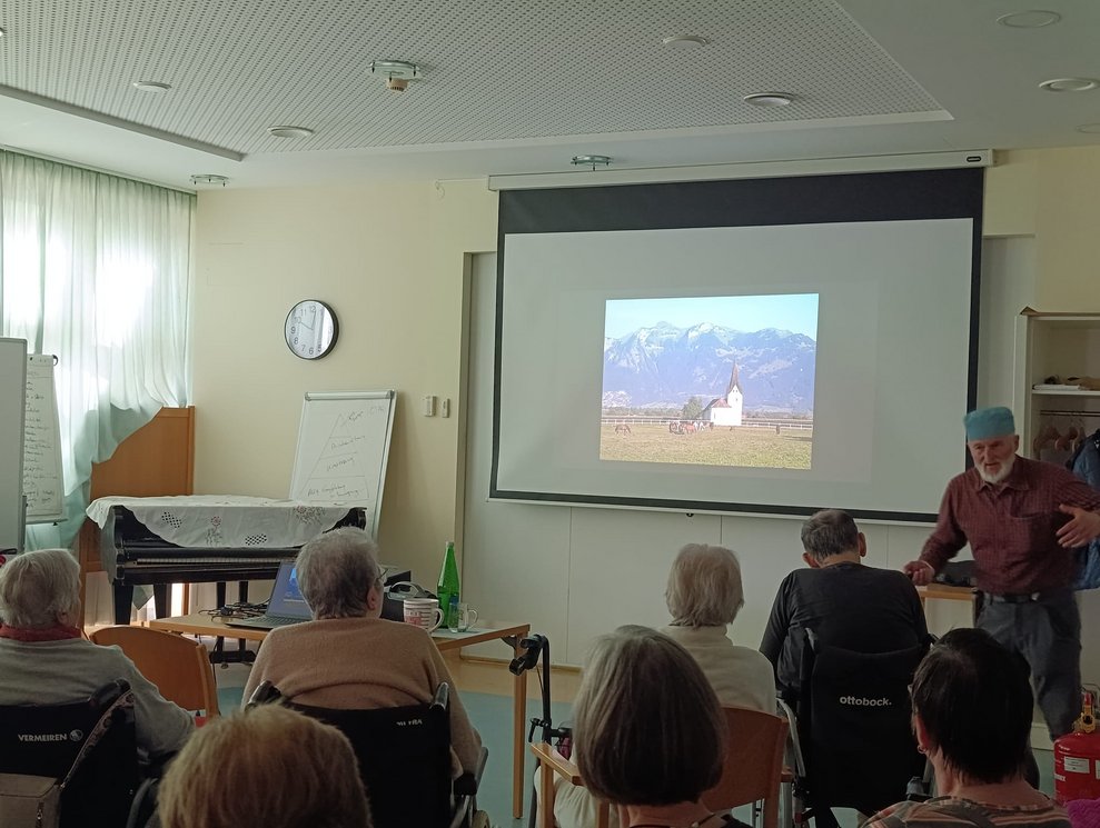 Foto auf Leinwand. Herr Gruber steht daneben. Viele BewohnerInnen.