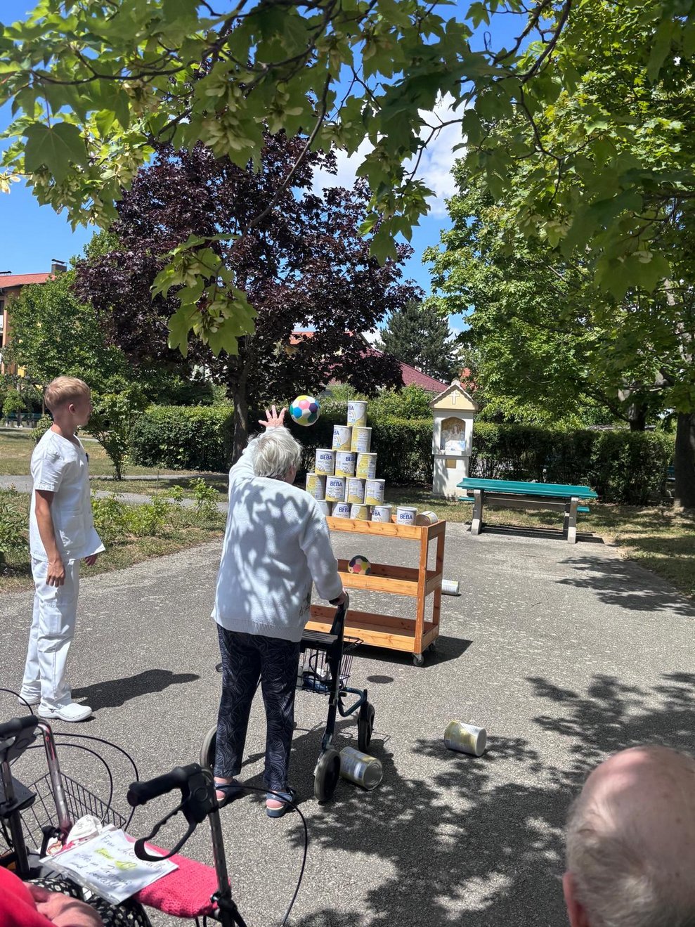 Bewohnerin beim Dosenschießen. Ball in der Luft. Mann (FSJ) steht daneben.