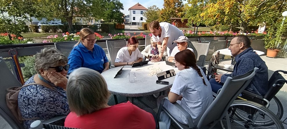 BewohnerInnen, Mann (Alltagsbegleiter), ehrenamtlich Tätige und zwei Praktikantinnen beim "Rummikub" spielen.