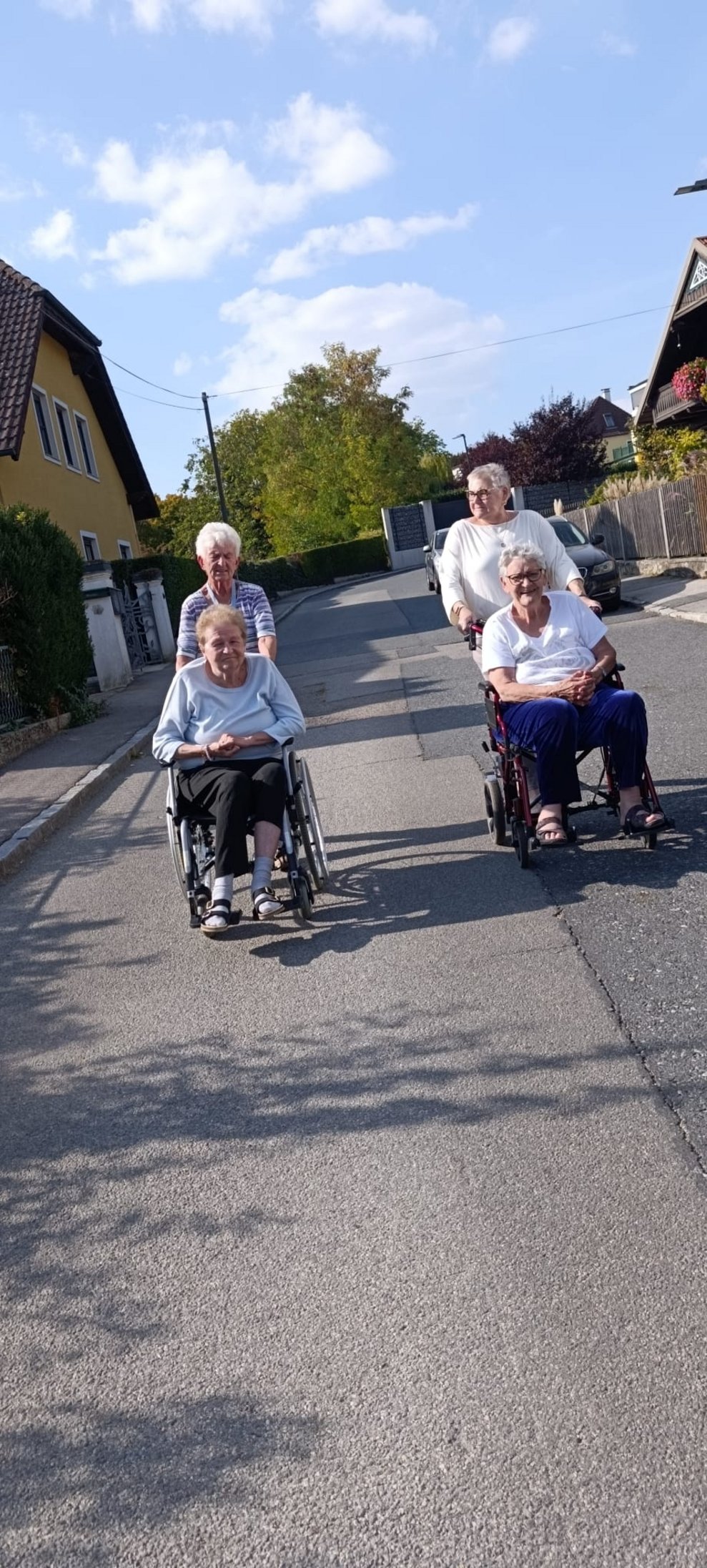 Zwei ehrenamtlich Tätige schieben Rollstühle mit Bewohnerinnen beim Spaziergang.