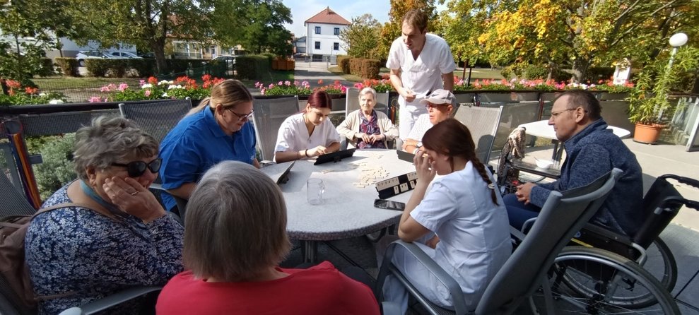 BewohnerInnen, Mann (Alltagsbegleiter), ehrenamtlich Tätige und zwei Praktikantinnen beim "Rummikub" spielen.