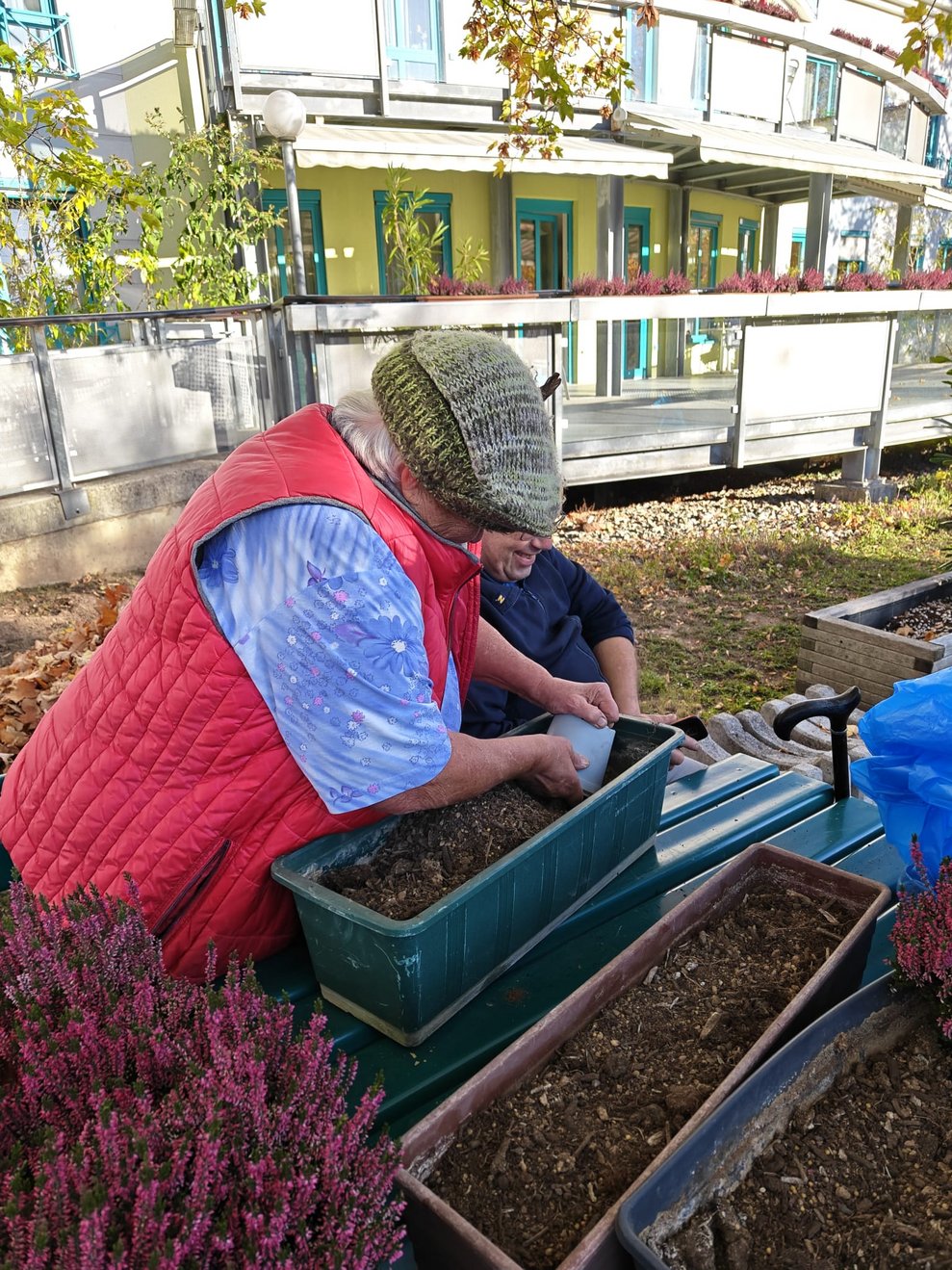 Bewohnerin hält leeren Plastik-Blumentopf ins Blumentrögerl.