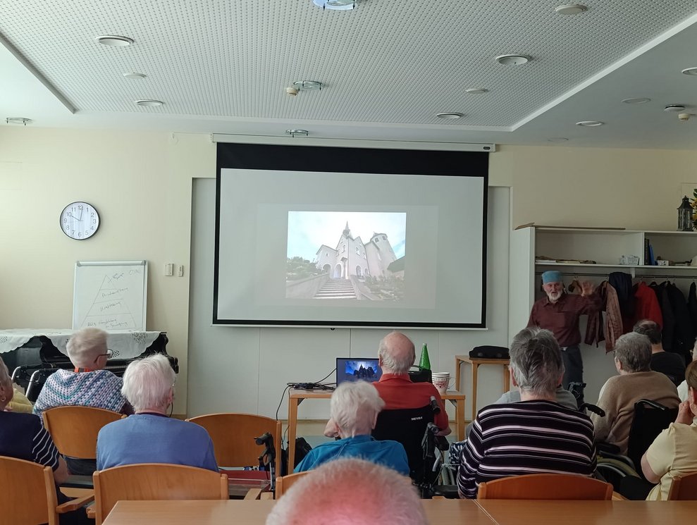 Foto auf Leinwand. Herr Gruber steht daneben. Viele BewohnerInnen.