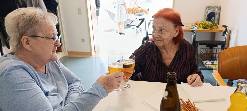 Zwei Bewohnerinnen stoßen mit zwei Gläser gefüllt mit Weißbier an.