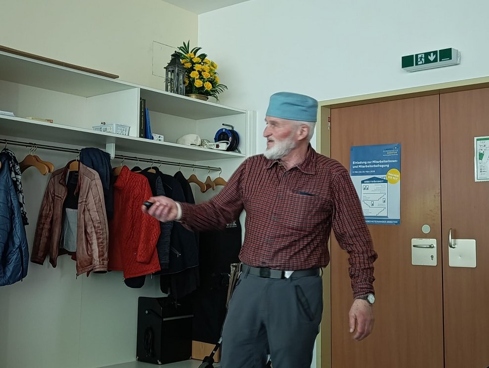 Herr Gruber steht tippt auf Fernbedienung.