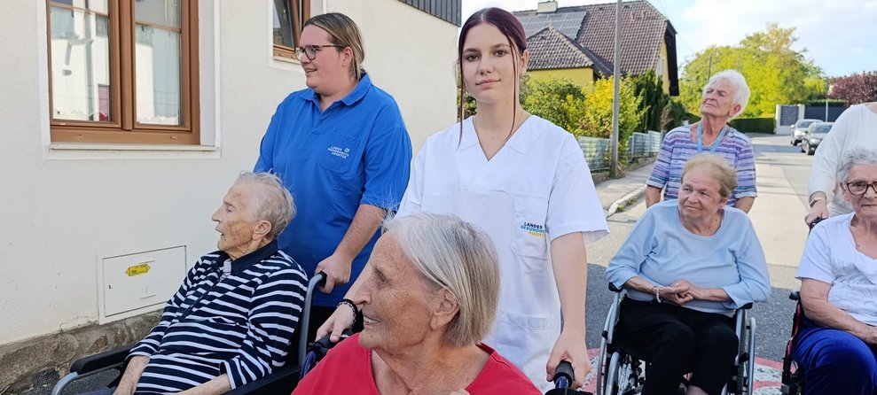Bwohnerinnen, Praktikantinnen und ehrenamtlich Tätige beim Spaziergang. Bewohnerinnen sitzen im Rollstuhl. Praktikantinnen und ehrenamtlich Tätige schieben Rollstuhl mit Bewohnerinnen.
