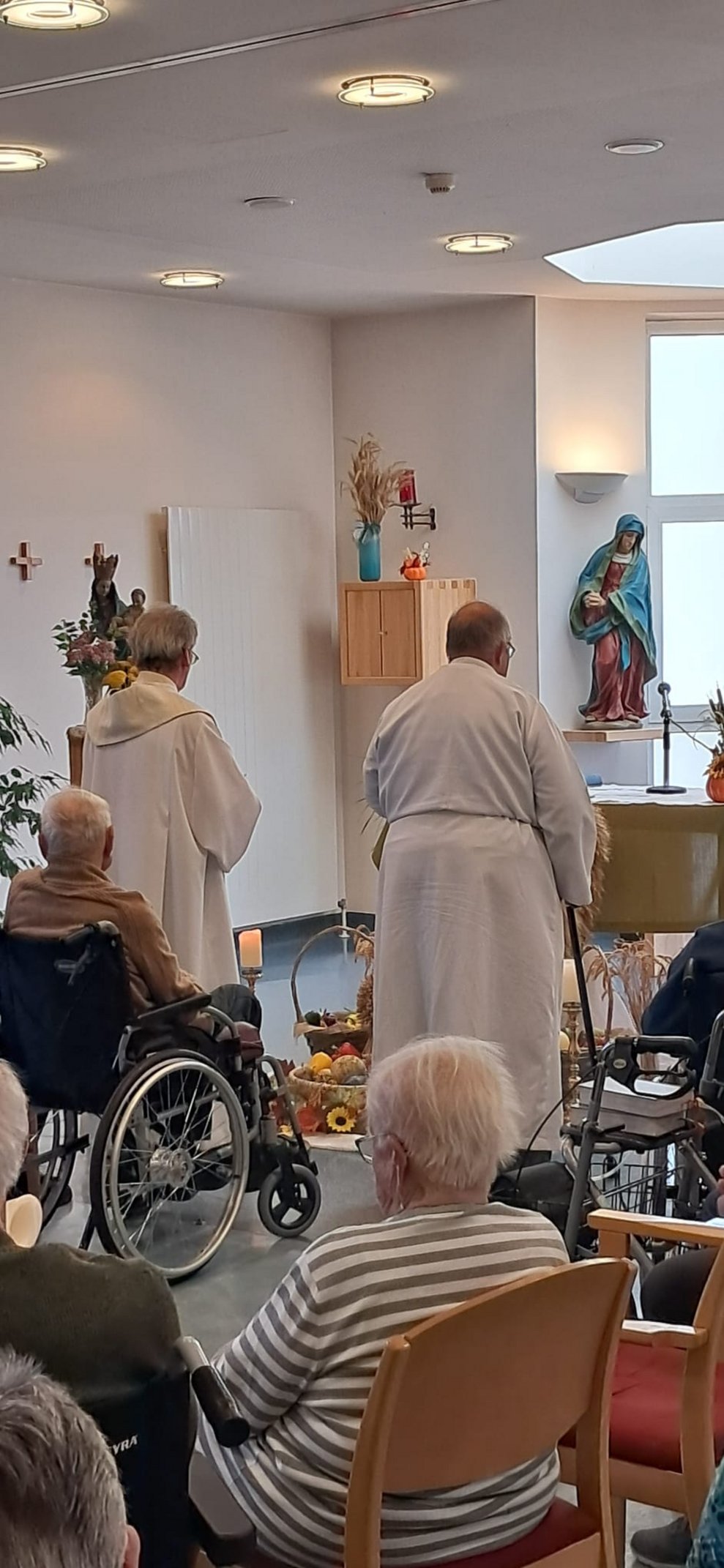 Zwei stehende Männer beim Altar. Sitzende Personen.