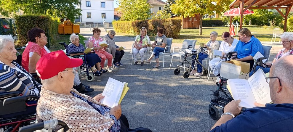 BewohnerInnen, Praktikantinnen und ehrenamtlich Tätige beim Singen. Alle halten Liederbuch in den Händen.
