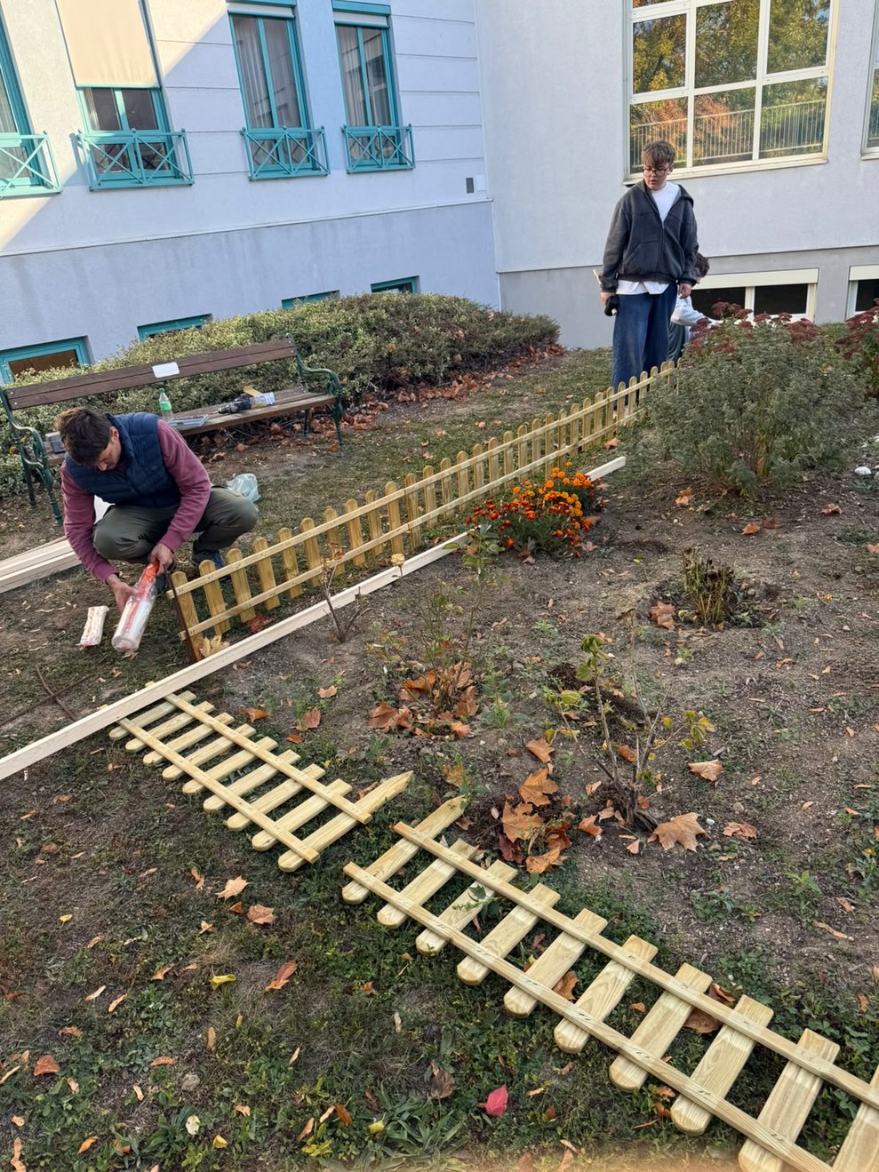 Lehrer und ein Schüler stellen Holzzaun um das Blumenbeet in unserem Garten auf.