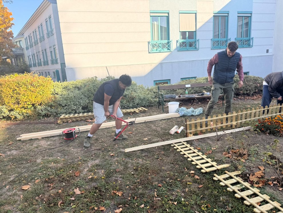Lehrer und zwei Schüler stellen Holzzaun um das Blumenbeet in unserem Garten auf.