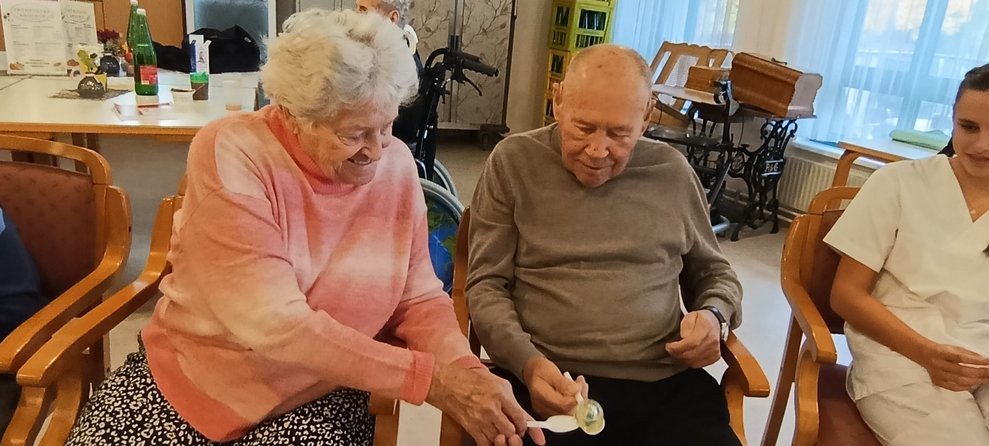 Zwei sitzende BewohnerIn halten Kochlöffel in der Hand und kleiner Ball liegt auf Kochlöffel.