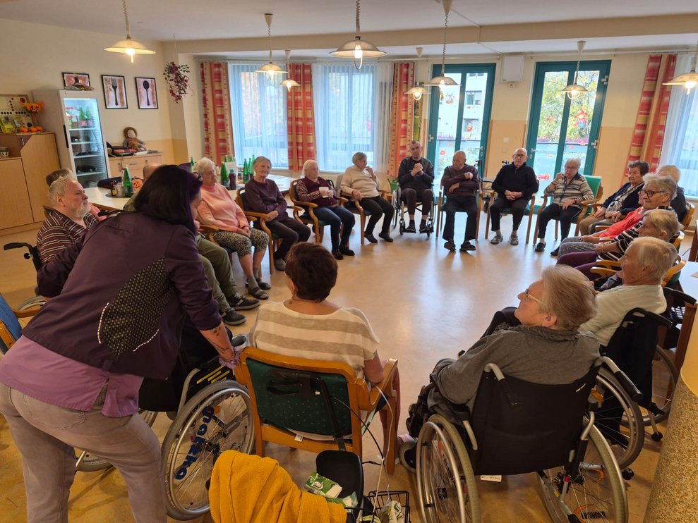 Sitzende BewohnerInnen bei der Bewegungsrunde. Alltagsbegleiterin steht gebückt.