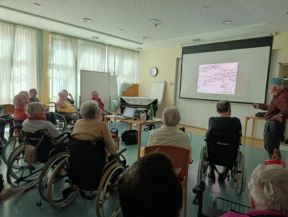 Foto auf Leinwand. Herr Gruber steht daneben. Viele BewohnerInnen.