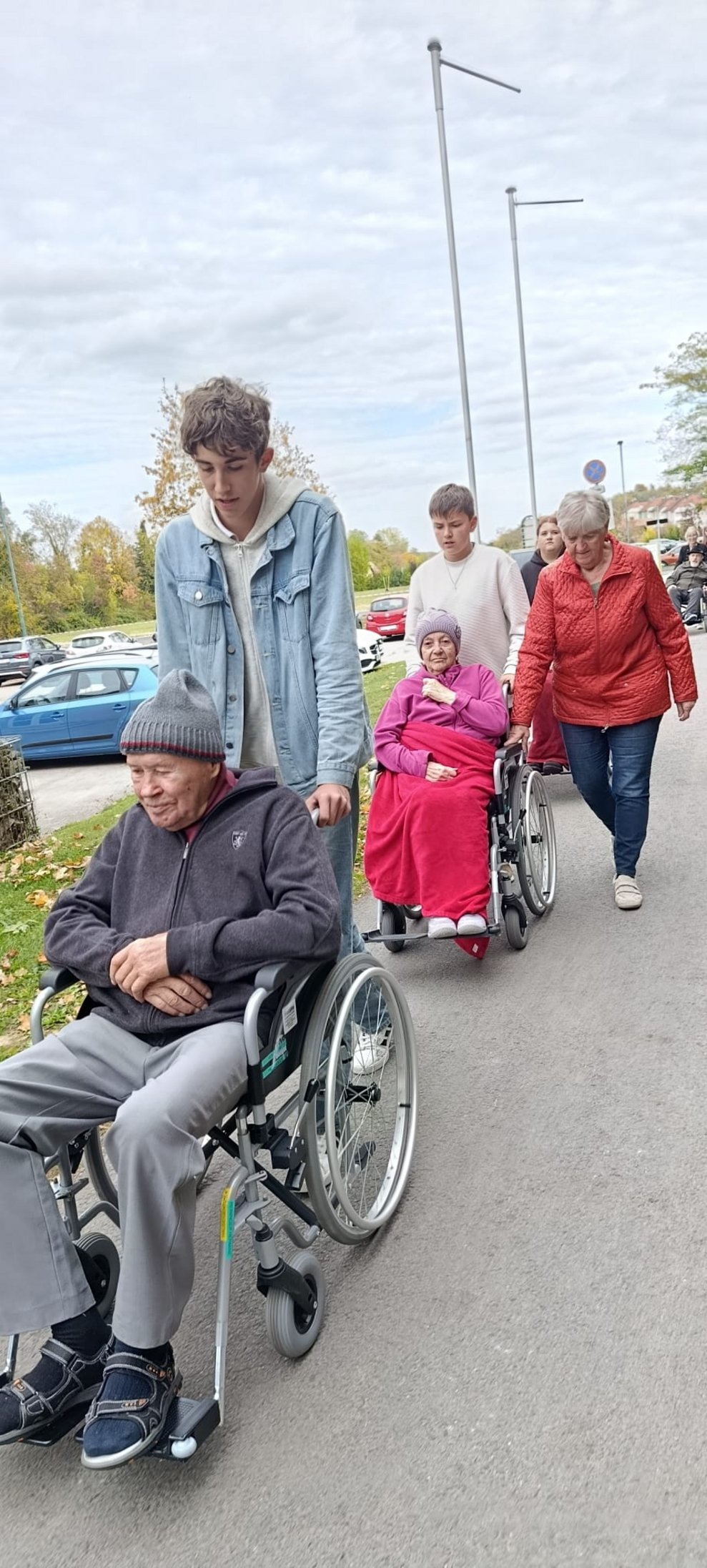 Schüler schieben Rollstuhl mit BewohnerIn. Ehrenamtlich Tätige geht daneben.