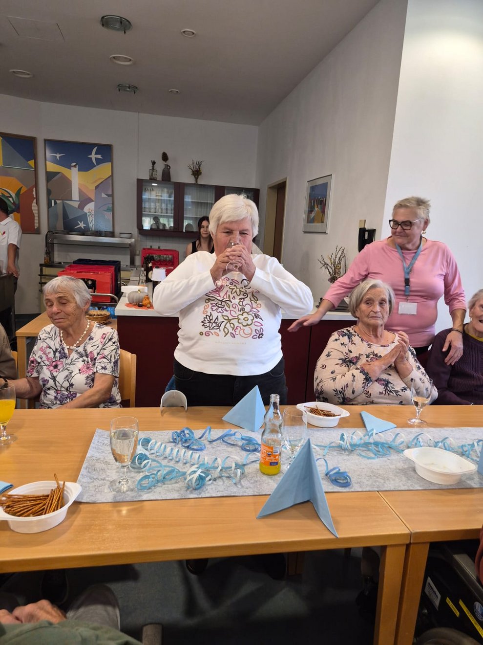 Personen beim Oktoberfest. Bewohnerin steht und trinkt aus Glas.