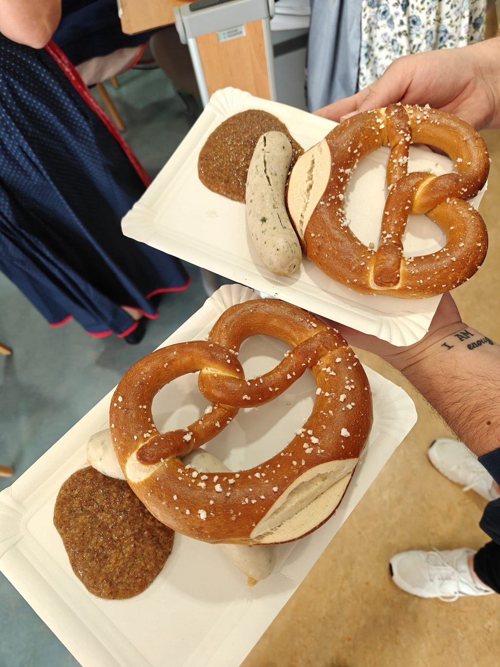 Hände halten zwei kleine Kartons mit jeweils Brezen, Weißwurst und Senf.
