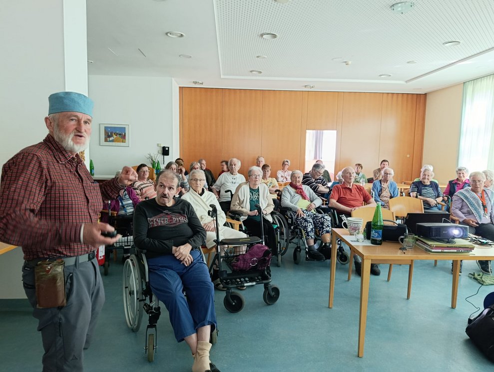 Herr Gruber steht. Viele BewohnerInnen.