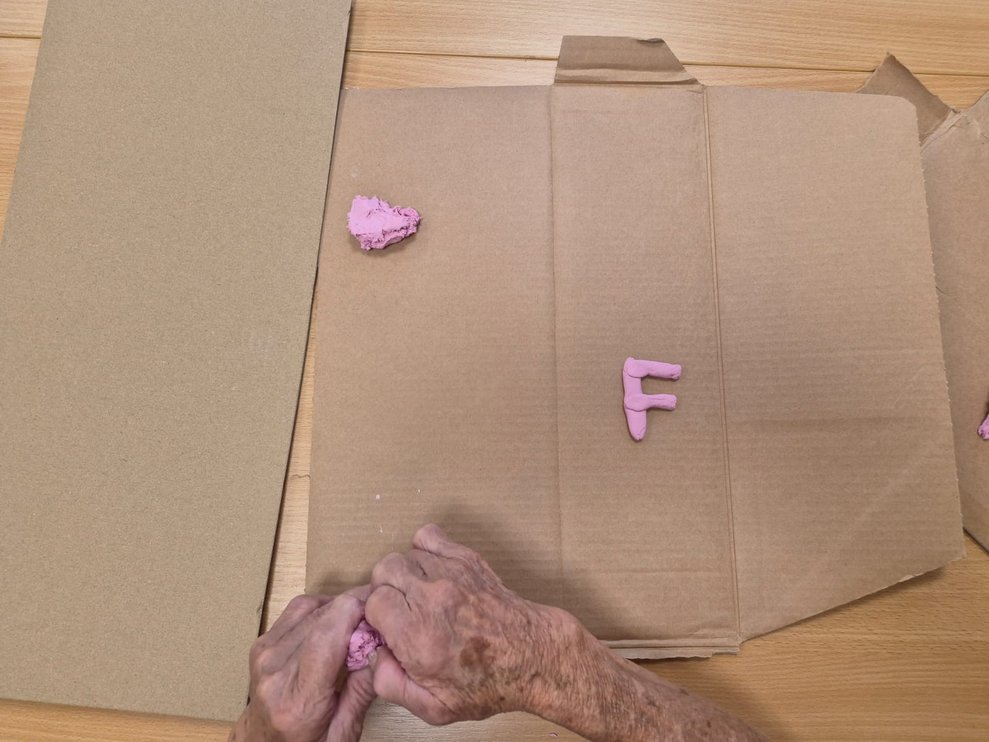 Hände kneten Ton. Buchstabe und ein kleiner Tonknödel liegt auf Karton.Kar
