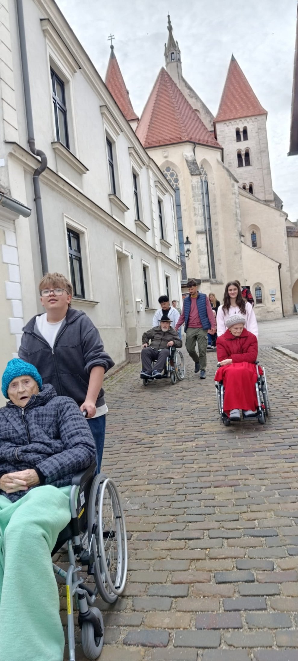 SchülerInnen schieben Rollstuhl mit BewohnerInnen. Personen gehen.