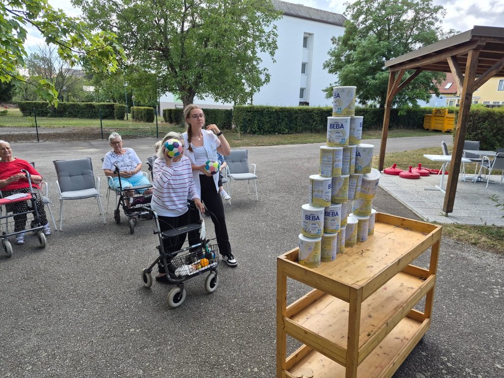 Bewohnerin beim Dosenschießen. Praktikantin steht daneben.