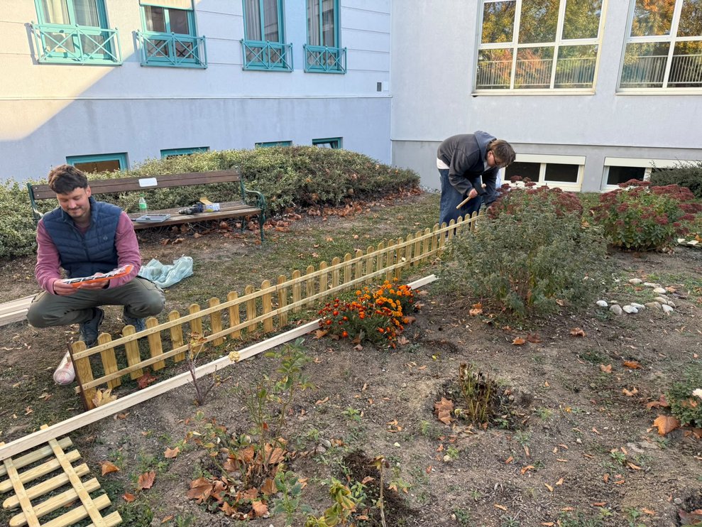 Lehrer und ein Schüler stellen Holzzaun um das Blumenbeet in unserem Garten auf.