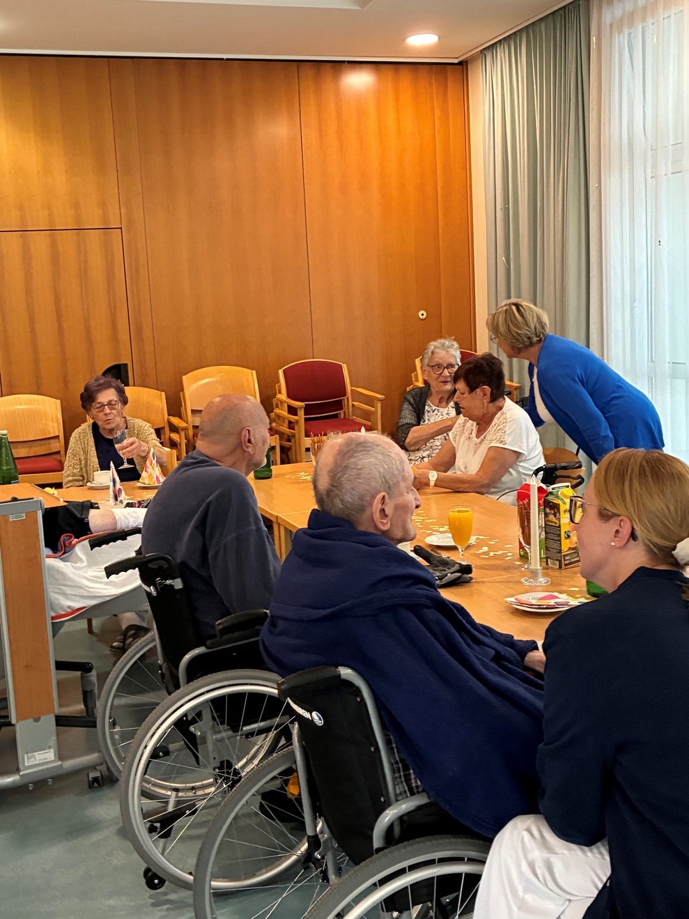 Personen sitzen beim Tisch. Eine Person steht.