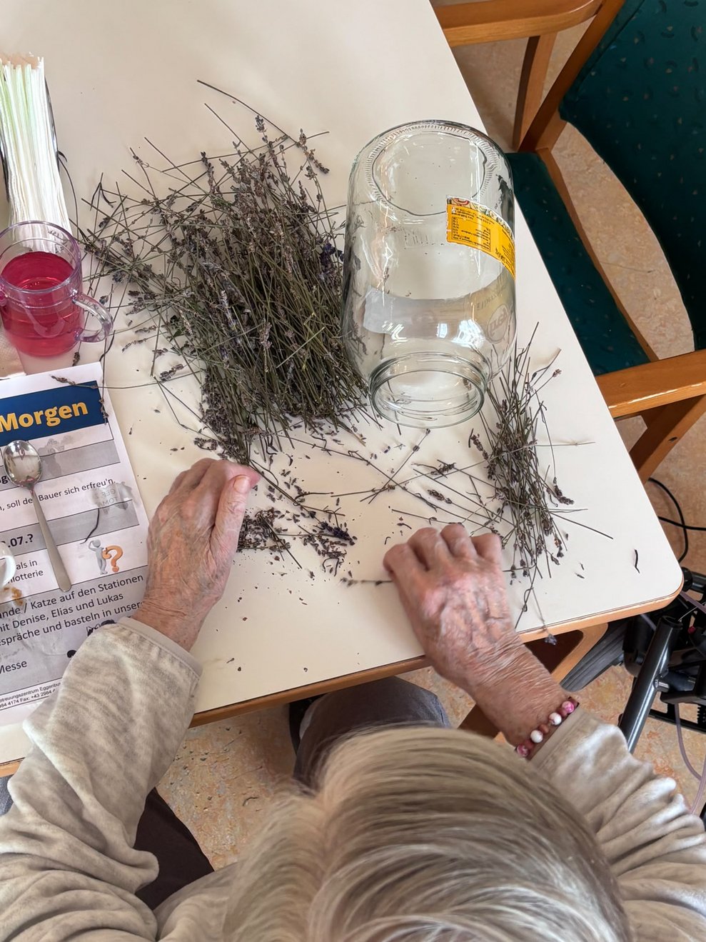 Bewohnerin rebelt Lavendel ab. Großes Glas steht auf Tisch.