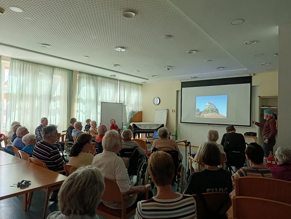 Foto auf Leinwand. Herr Gruber steht daneben. Viele BewohnerInnen.