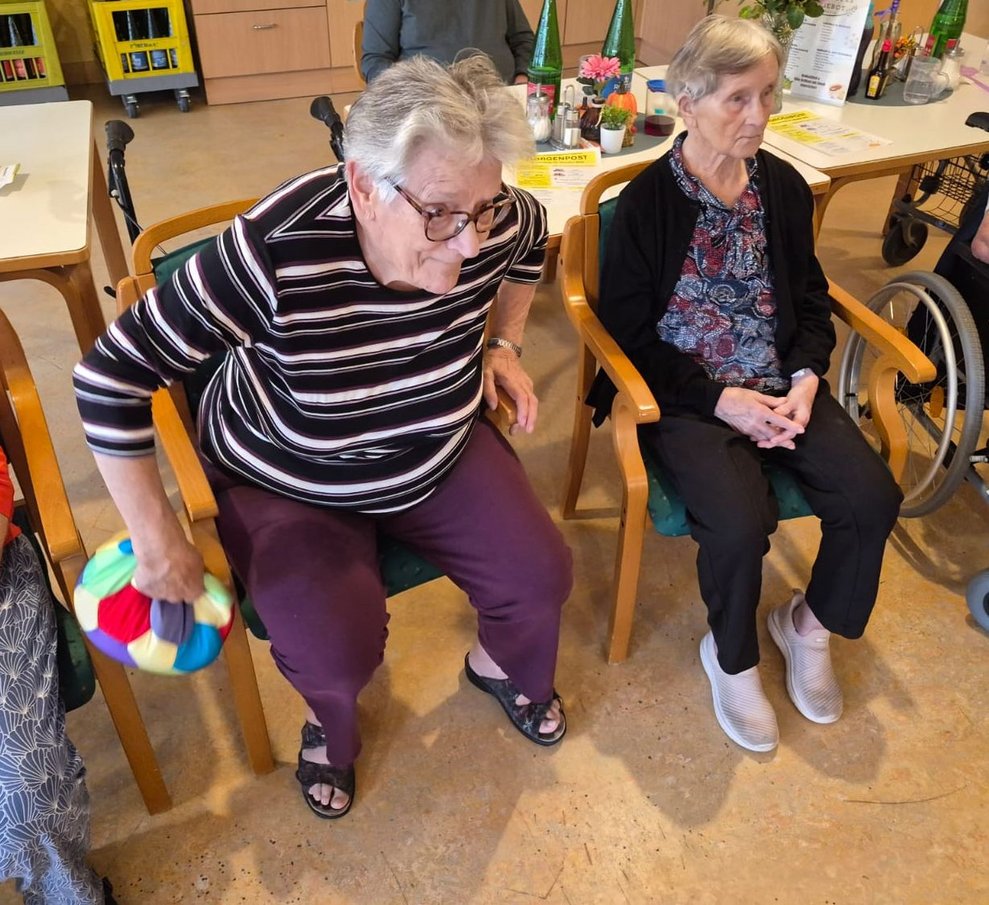 Sitzende Bewohnerin hält Stoffball in der Hand. Bewohnerin sitzt daneben.