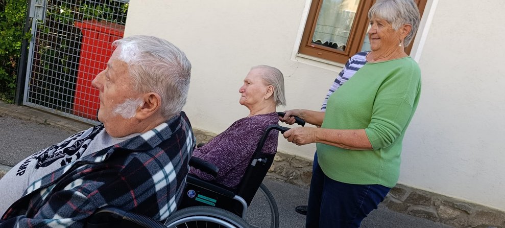 Bewohner beim Spaziergang im Rollstuhl. Ehrenamtlich Tätige schiebt Rollstuhl mit Bewohnerin.