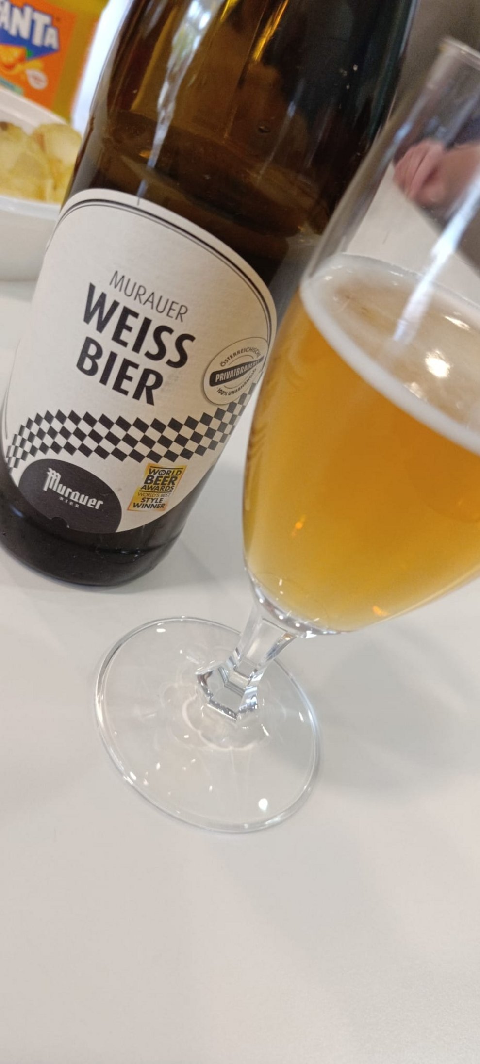 Flasche Weißbier und Glas gefüllt mit Weißbier steht auf Tisch.