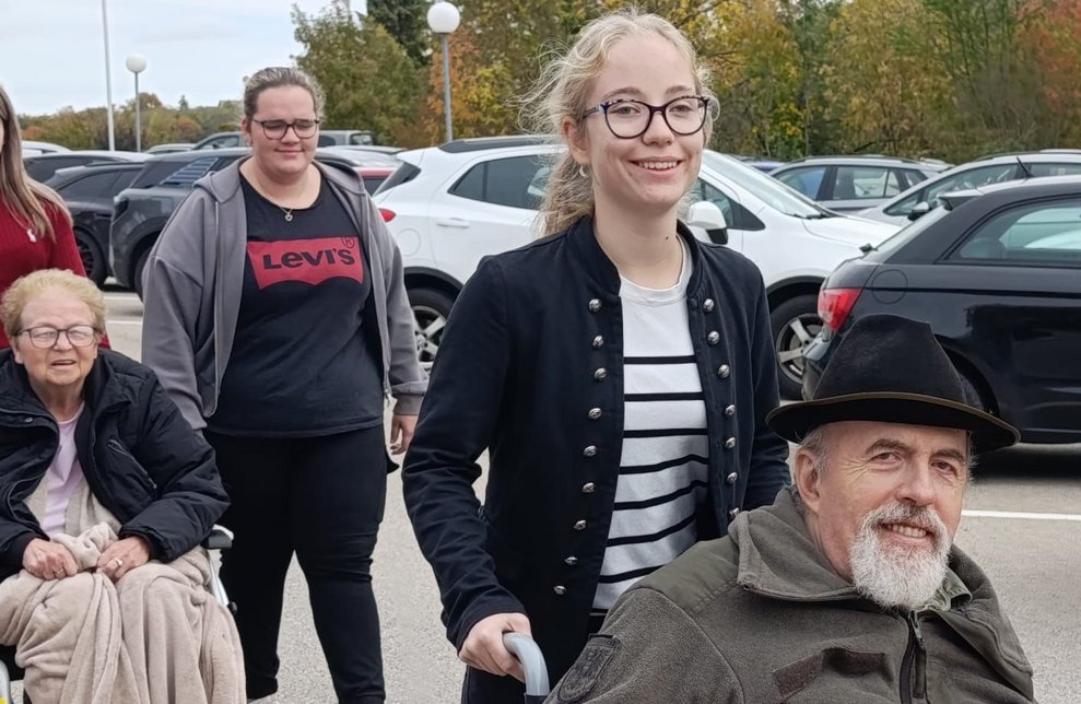 Schülerin schiebt Rollstuhl mit Bewohner. Bewohnerin sitzt im Rollstuhl. Schülerin geht daneben.