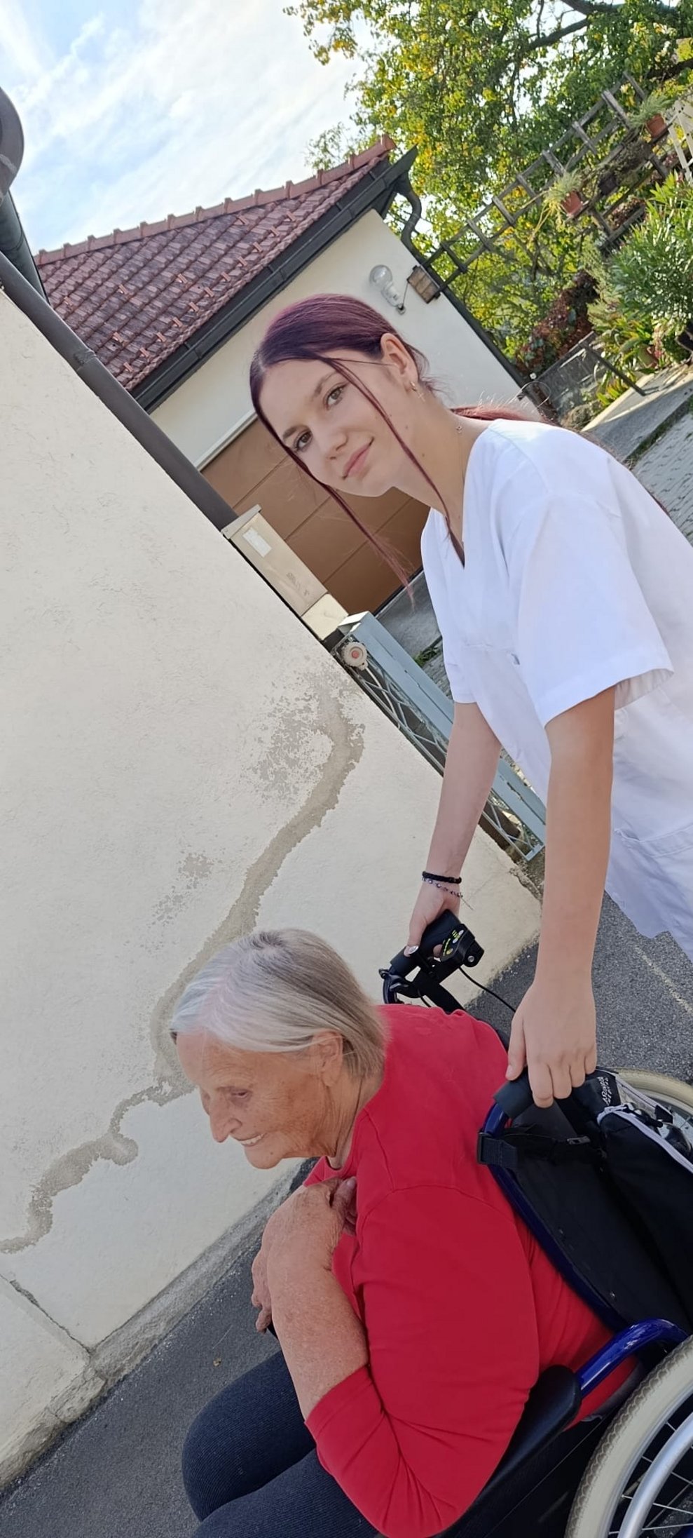 Praktikantin schiebt Rollstuhl mit Bewohnerin beim Spaziergang.