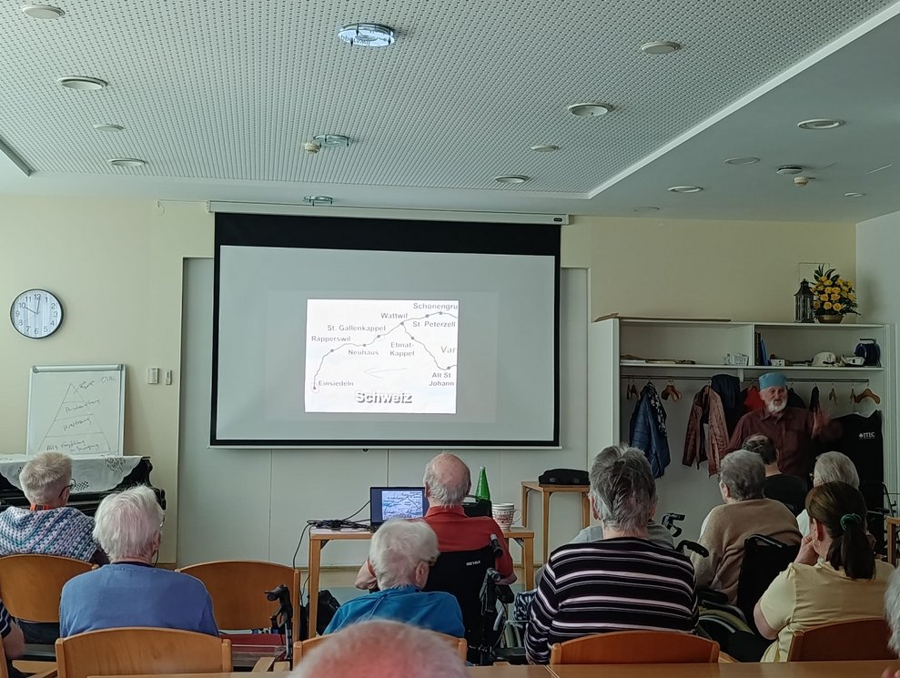 Foto auf Leinwand. Herr Gruber steht daneben. Viele BewohnerInnen.