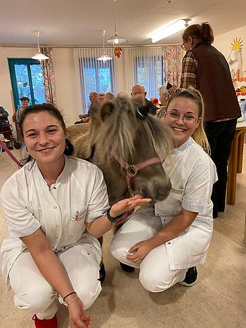 Zwei lächelnde Mitarbeiterinnen mit braunem Pony. 