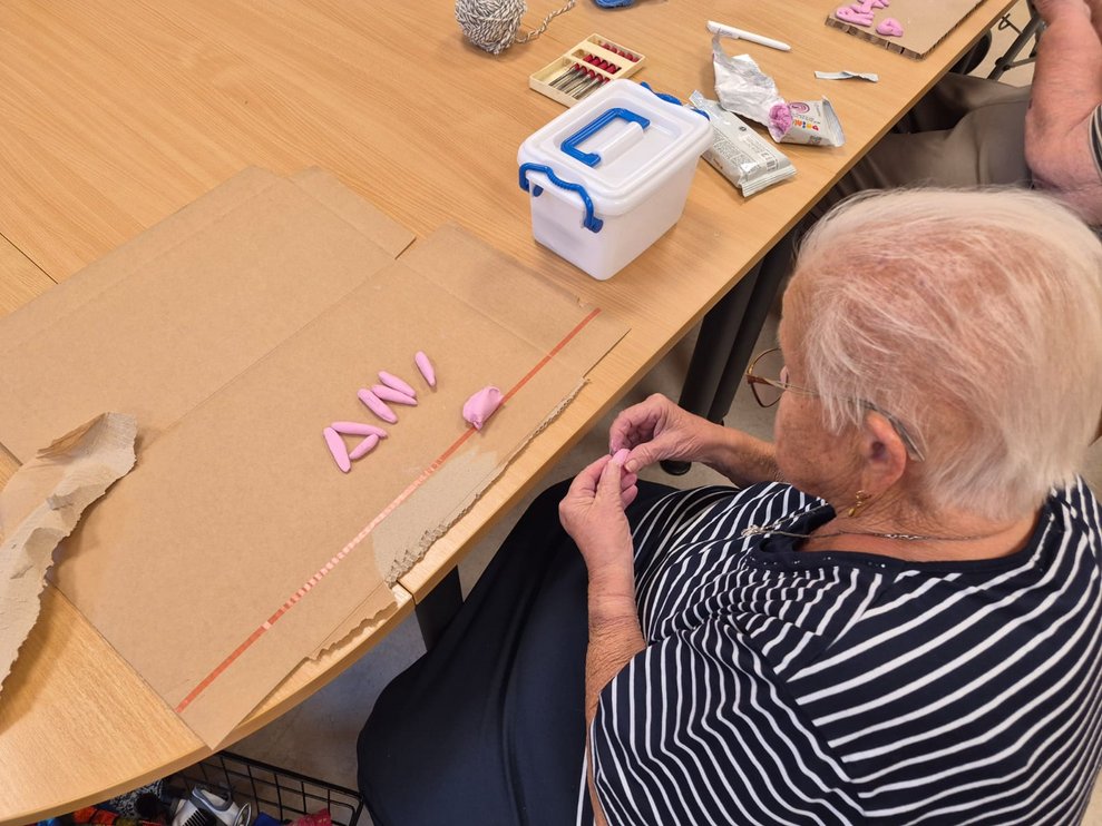 Bewohnerin formt Ton mit Hände. Buchstaben aus Ton liegen auf Karton.