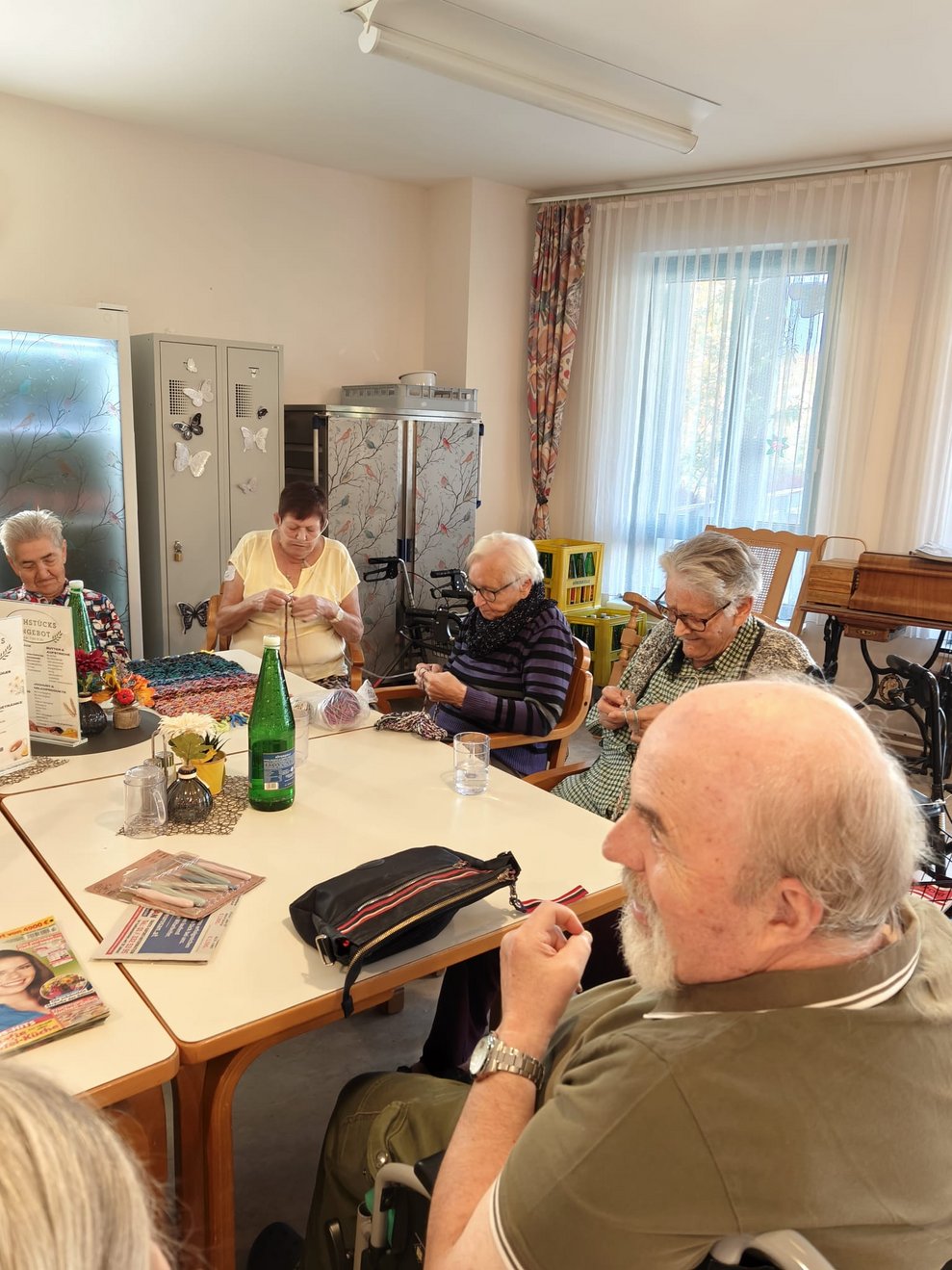 Bewohnerinnen beim Häkeln und Stricken. Bewohner schaut zu.