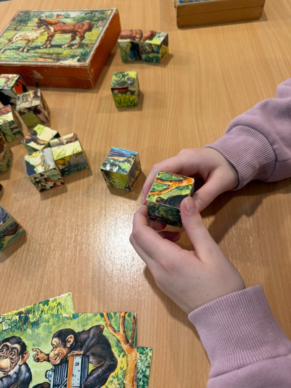 Hände halten einen Würfelpuzzle in der Hand. Teile des Würfelpuzzles liegen auf Tisch.
